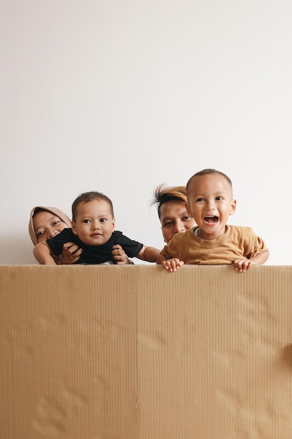 Feliz família muçulmana asiática escondida atrás de caixa de papelão em casa