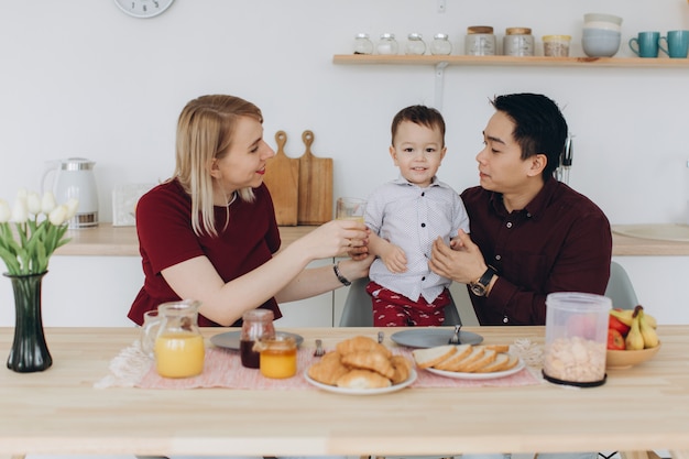 Feliz família multicultural. Pai asiático e sua esposa loira caucasiana tomar café da manhã com seu lindo filho na cozinha.