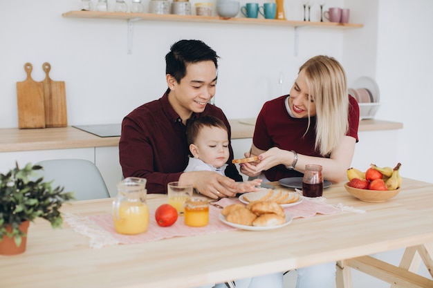 Feliz familia multicultural. Papá asiático y su esposa rubia caucásica desayunan con su hermoso hijo en la cocina.