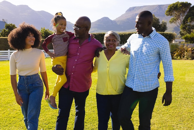 Feliz familia multirracial multigeneración caminando sobre un campo de hierba contra las montañas en el patio