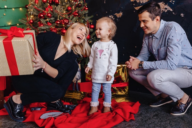 Feliz familia con un niño celebra el año nuevo cerca del árbol de Navidad