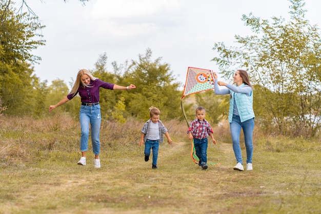 Feliz familia no tradicional de dos jóvenes madres y sus hijos lanzan una cometa sobre la naturaleza al atardecer