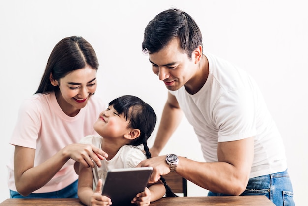 Feliz família pai e mãe com a filha sentada e olhando para o computador tablet juntos na sala de estar em casa