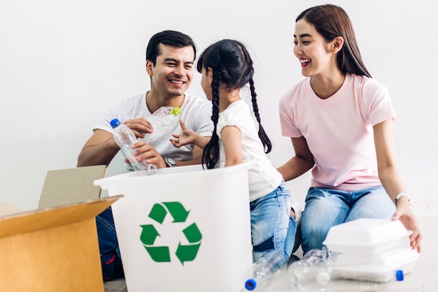 Feliz familia sonriente divirtiéndose poniendo botellas de plástico y papel vacíos en la caja de reciclaje