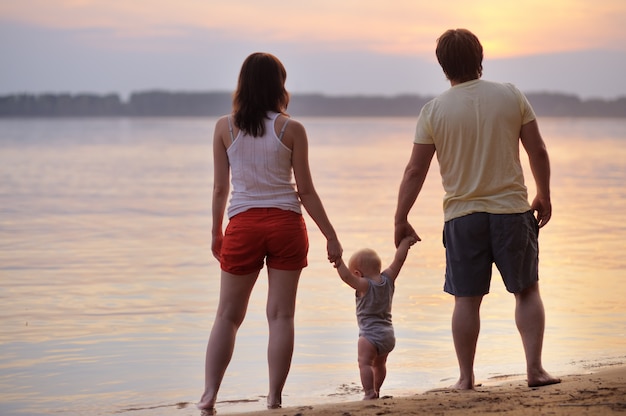 Feliz familia de tres en la playa al atardecer