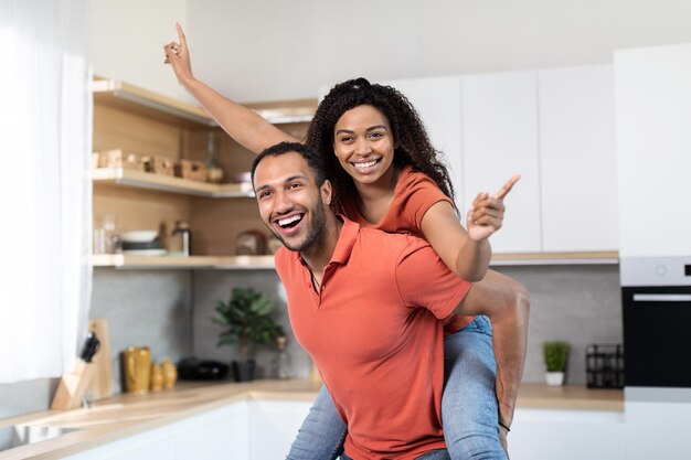 Foto feliz feliz e atraente jovem marido negro em camiseta vermelha segurando a esposa nas costas divirta-se aproveite o tempo livre