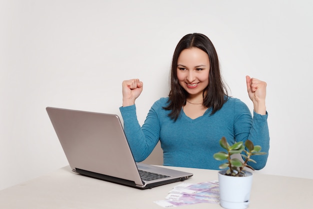 Feliz feliz mujer contenta sentada en su computadora portátil. El concepto de éxito, trabajo independiente, ganancias remotas, tecnología informática, lotería, ganar