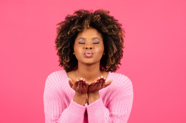 Feliz fêmea afro-americana encaracolada do milênio em casual com os olhos fechados mandando beijo