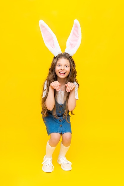 Feliz feriado da Páscoa Uma linda garotinha com orelhas de coelho na cabeça comemorando um dia de primavera A criança retrata um coelho em um fundo amarelo isolado