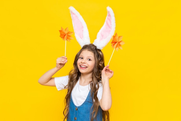 Feliz feriado da Páscoa Uma linda garotinha com orelhas de coelho na cabeça comemorando um dia de primavera Uma criança em um vestido de verão segura flores de origami em um fundo amarelo isolado