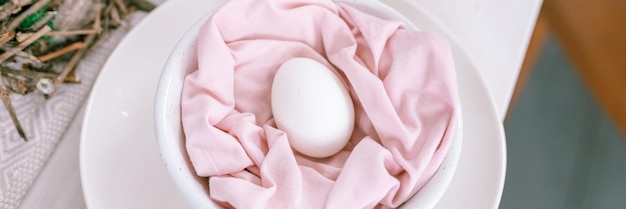Feliz feriado de páscoa na temporada de primavera decoração festiva para casa comida tradicional ovo de galinha branco natural em tecido rosa pastel em um prato no banner da mesa