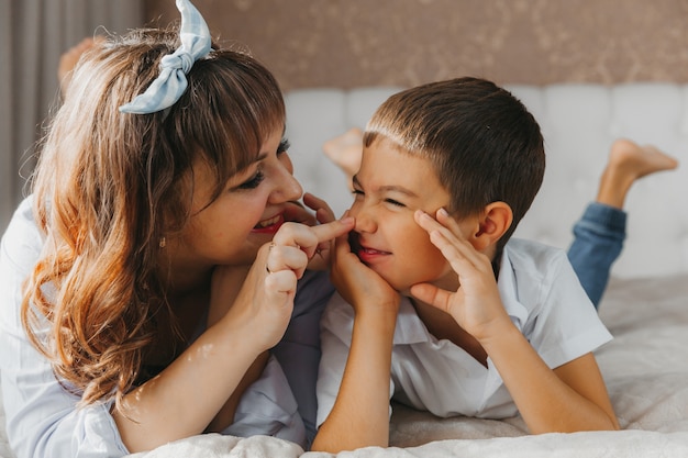 Feliz filho e mãe deitar na cama e rir. Dia das Mães!