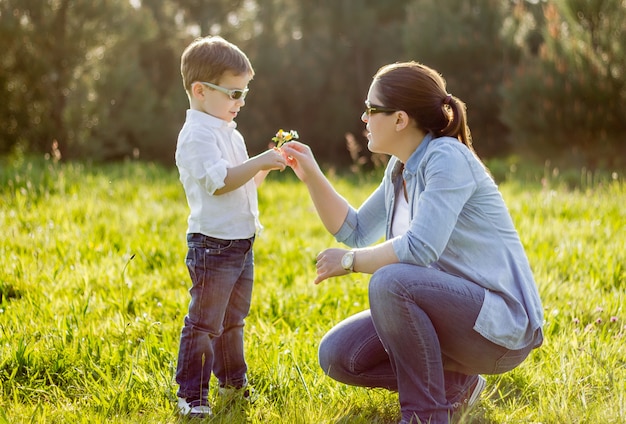 Feliz filho fofo dando um buquê de flores para sua mãe em um campo ensolarado