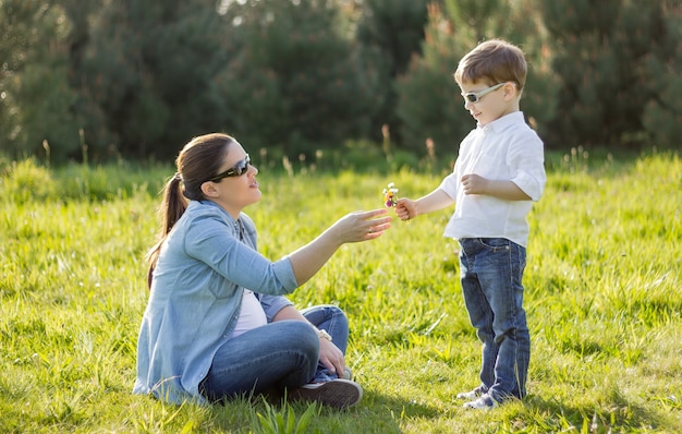 Feliz filho fofo dando um buquê de flores para sua mãe grávida em um campo ensolarado