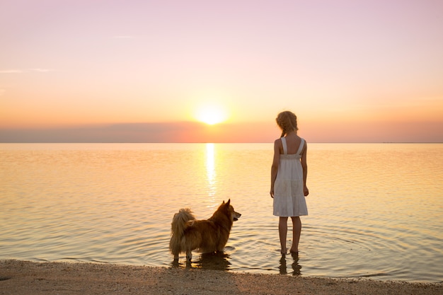 Feliz fim de semana à beira-mar - a menina está andando com um cachorro corgi à beira-mar ao pôr do sol. Paisagem ucraniana no Mar de Azov, Ucrânia