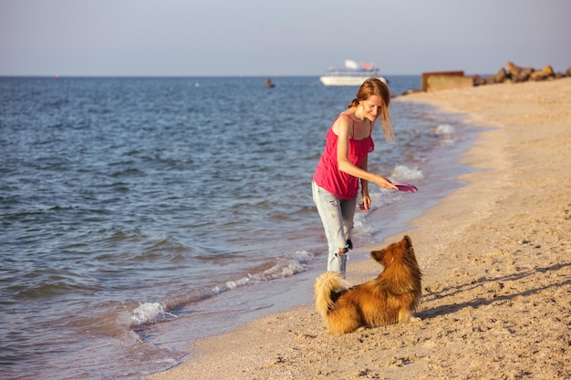 Feliz fim de semana divertido à beira-mar - garota brincando no frisbee com um cachorro na praia. Verão