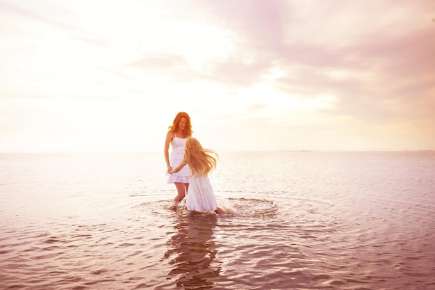 Feliz fin de semana divertido junto al mar: mamá e hija vestidas de blanco dando vueltas junto al mar al atardecer. Paisaje ucraniano en el mar de Azov, Ucrania