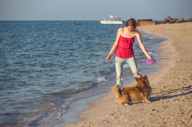 Feliz fin de semana divertido junto al mar - niña jugando en el frisbee con un perro en la playa. Verano