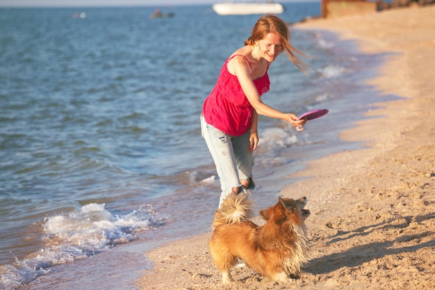 Feliz fin de semana divertido junto al mar - niña jugando en el frisbee con un perro en la playa. Verano