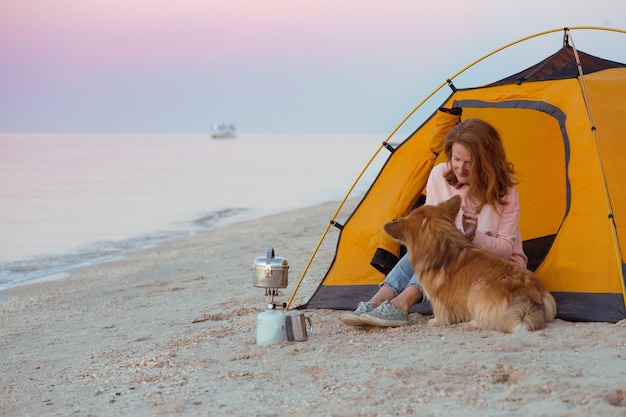 Feliz fin de semana junto al mar - chica con un perro en una tienda de campaña en la playa al amanecer. Paisaje ucraniano en el mar de Azov, Ucrania