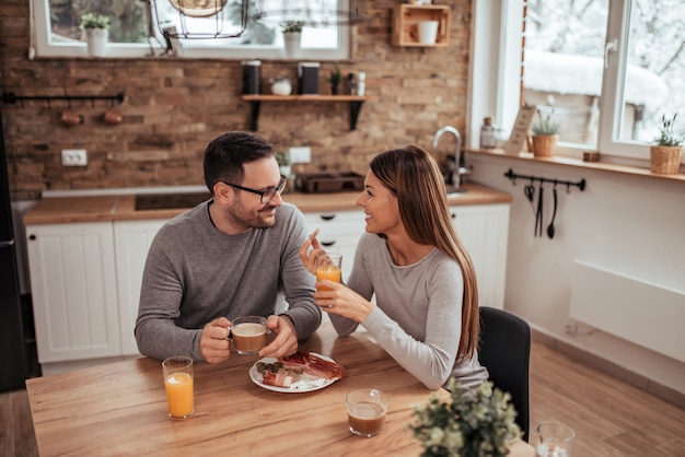 Feliz fin de semana. Pareja positiva que se sienta en la cocina rústica moderna, tomando café por la mañana y desayunando.