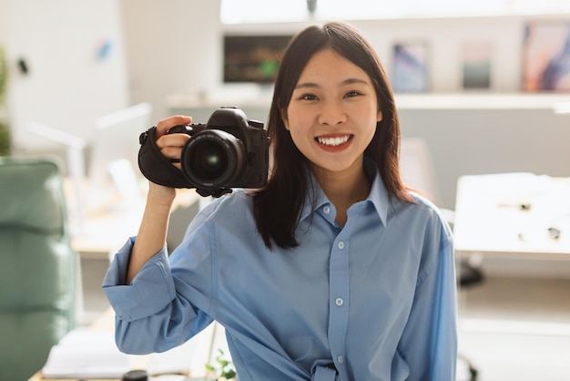 Feliz fotógrafa china tomando fotos sosteniendo la cámara en casa