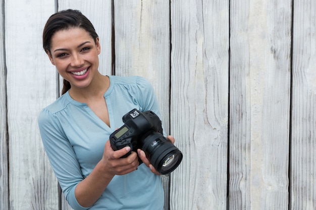 Feliz fotógrafo feminino em pé contra um fundo de madeira