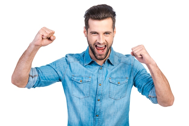 Feliz ganador. Feliz joven apuesto gesticulando y manteniendo la boca abierta mientras está de pie contra el fondo blanco.