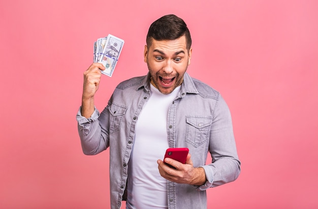 Feliz ganador Hombre emocionado en camiseta casual con mucho dinero en monedas de dólar y teléfono celular en las manos