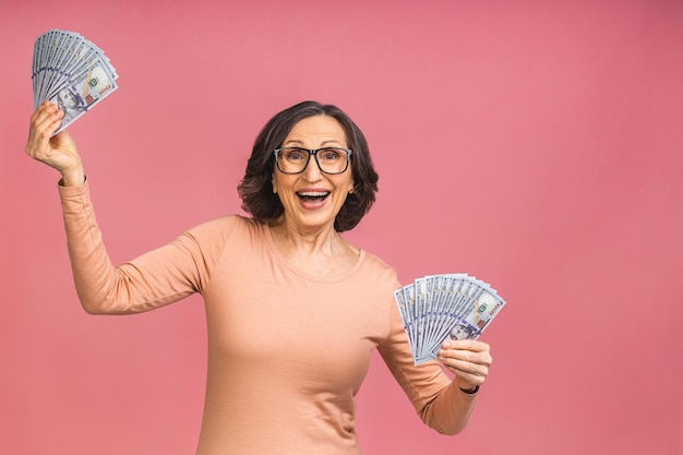 ¡Feliz ganador! Imagen de una anciana feliz senior madura que se encuentran aisladas sobre fondo rosa, sosteniendo dinero.