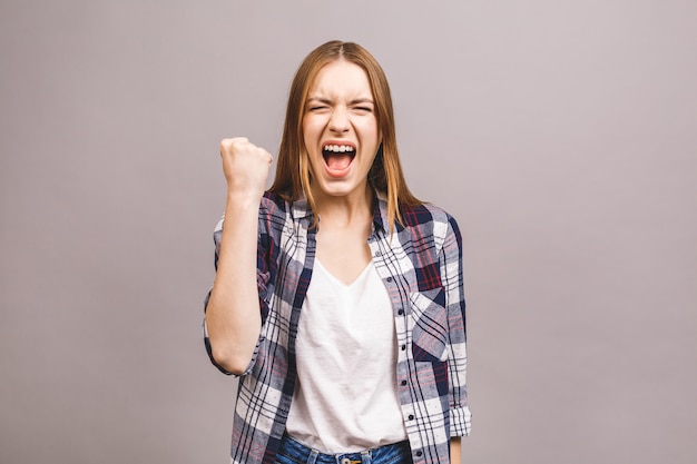 Feliz ganador! Primer de la mujer atractiva joven emocional con mantener las manos en los puños, aislado en la pared gris. Mujer joven sorprendida gritando.