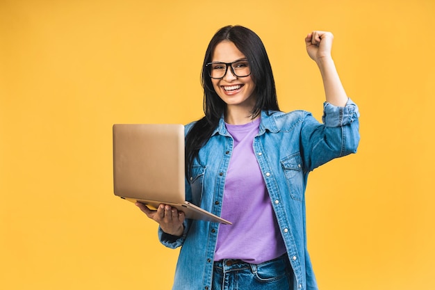 Feliz ganador Retrato de atractiva mujer de negocios sonriente emocionada sorprendida con portátil aislado sobre fondo amarillo Ganador con éxito