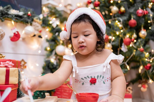 Feliz garotinha asiática cozinhando pão de gengibre em casa com os pais para o dia de Natal. Biscoitos de Natal caseiros para criança.