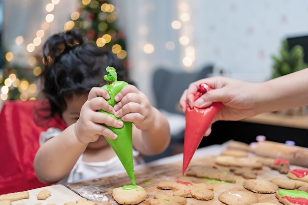 Feliz garotinha asiática cozinhando pão de gengibre em casa com os pais para o dia de Natal. Biscoitos de Natal caseiros para criança.