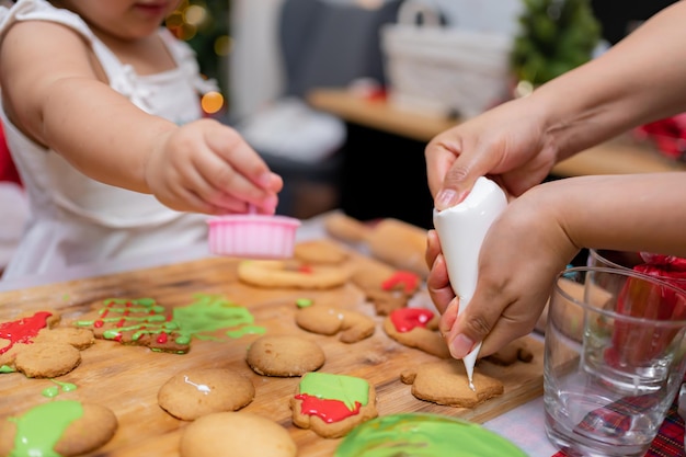 Feliz garotinha asiática cozinhando pão de gengibre em casa com os pais para o dia de Natal. Biscoitos de Natal caseiros para criança.