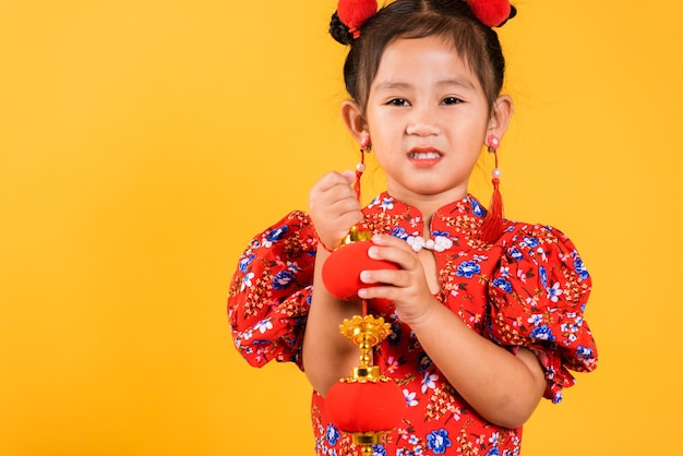 Feliz garotinha chinesa asiática sorrindo usando cheongsam qipao vermelho segurando lanternas de seda