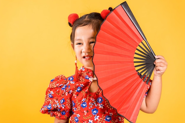 Feliz garotinha chinesa asiática sorrindo usando cheongsam vermelho segurando fã