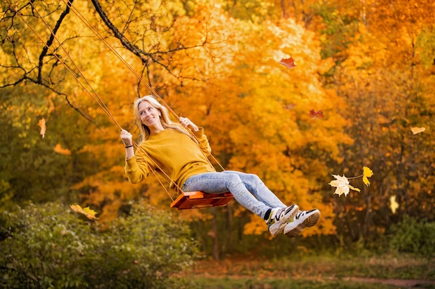 Feliz garotinha loira caucasiana sorrindo e andando de corda no outono no parque