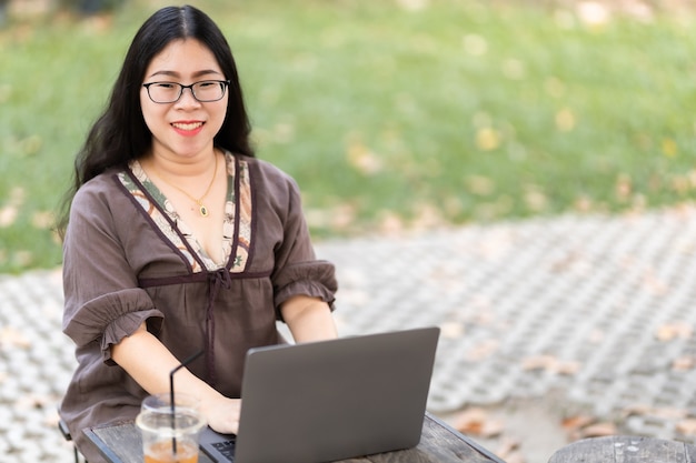 Feliz de la gente asiática autónoma de negocios casual femenino trabajando con computadora portátil con taza de café y teléfono inteligente en la cafetería como el fondo, el concepto de comunicación