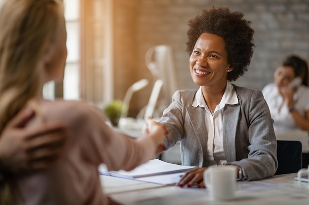 Foto feliz gerente de banco afro-americano apertando as mãos de seus clientes após a reunião no escritório