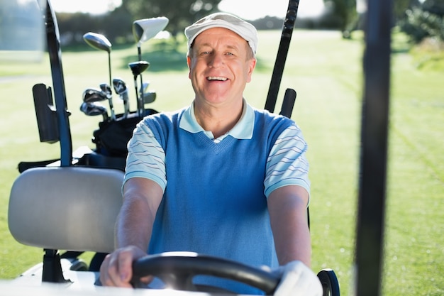 Feliz golfista conduciendo su buggy de golf sonriendo a la cámara