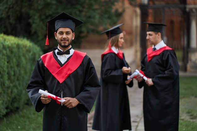 Feliz graduado indio en bata de graduación tiene un diploma en el campus.