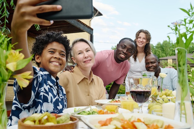 Feliz grande família intercultural olhando para a câmera do smartphone segurado por um lindo garoto sorridente sentado na frente de seus pais e avós