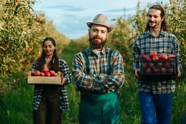 Feliz granjero barba bigote sombrero manos en el pecho mujer hombre trabajadores llevan manzanas