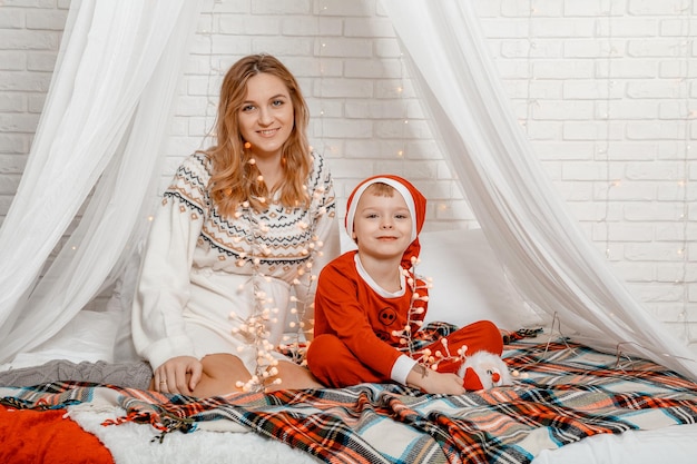 Feliz grávida mãe e filho olhando para a câmera no Natal, deitado em um sofá na cama. Decoração de ano novo. Mãe e filho grávidos estão conversando e passando um tempo juntos na cama em casa.