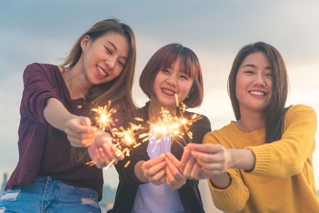 Feliz grupo de amigas asiáticas disfrutar y jugar luces de Bengala en la parte superior del techo al atardecer de la tarde