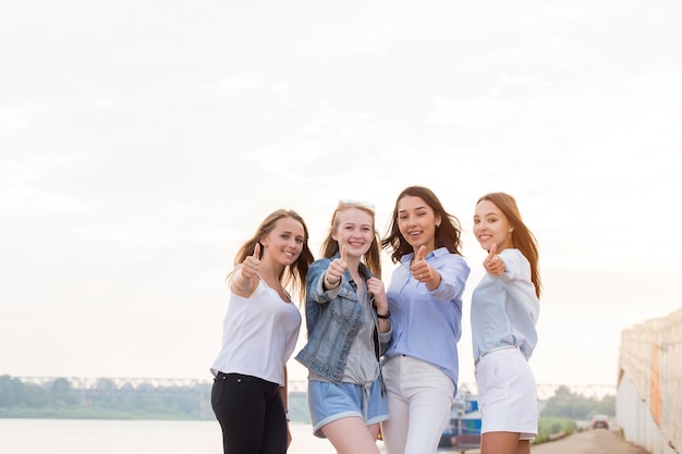 Feliz grupo de amigas con los pulgares hacia arriba al aire libre mirando a la cámara y sonriendo