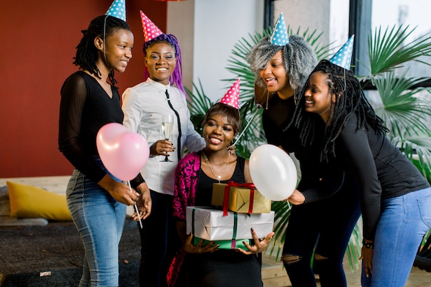 Feliz grupo de chicas africanas con coloridos regalos y globos en las manos mirando a la cámara y sonriendo