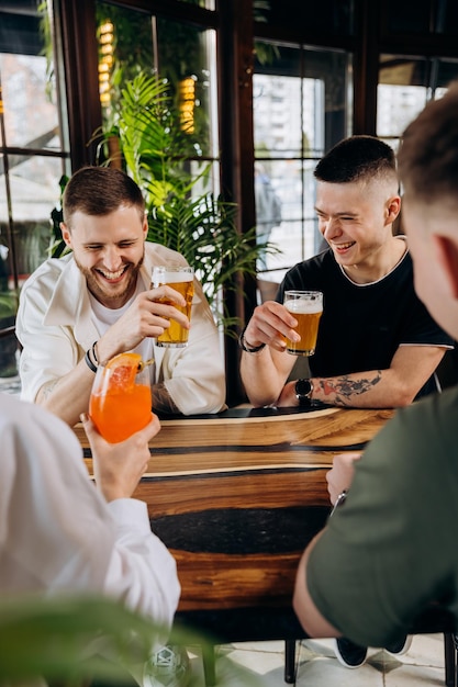 Feliz grupo de amigos bebendo e tilintando com cerveja e coquetéis no restaurante bar da cervejaria