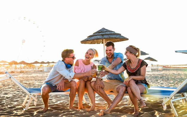 Feliz grupo de amigos do milênio se divertindo na festa na praia bebendo coquetéis chiques ao pôr do sol